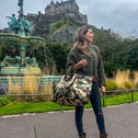 Woman standing in front of Edinburgh castle wearing a medium-sized tote bag with an army print and sequin detailing, predominantly in shades of green, gold, brown, and grey.