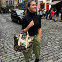 Woman standing in Edinburgh on the street, wearing a small tote bag featuring an army print with sequins, in green, brown, and beige colors