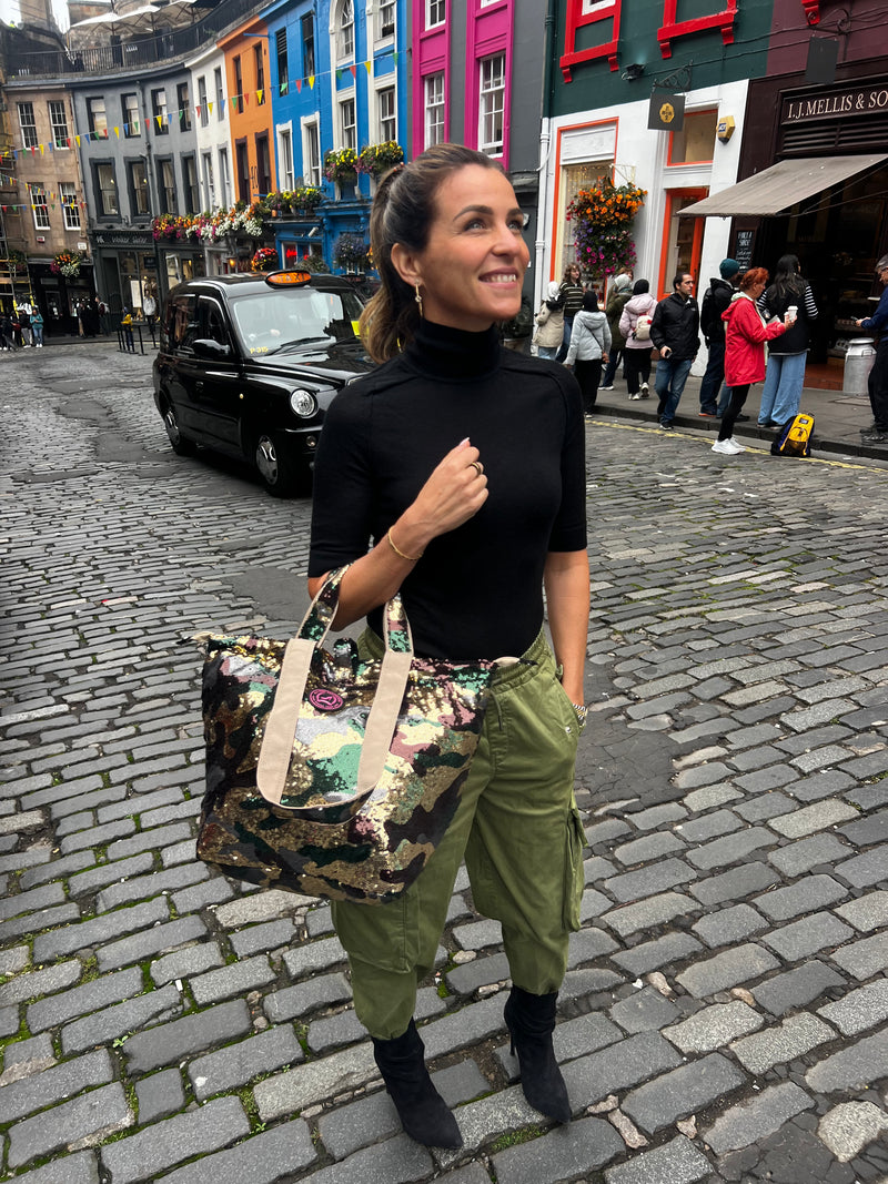 Woman standing in Edinburgh on the street, wearing a small tote bag featuring an army print with sequins, in green, brown, and beige colors
