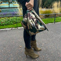 A toiletry bag ion hand with an army print and sequins, predominantly green, brown, and beige.