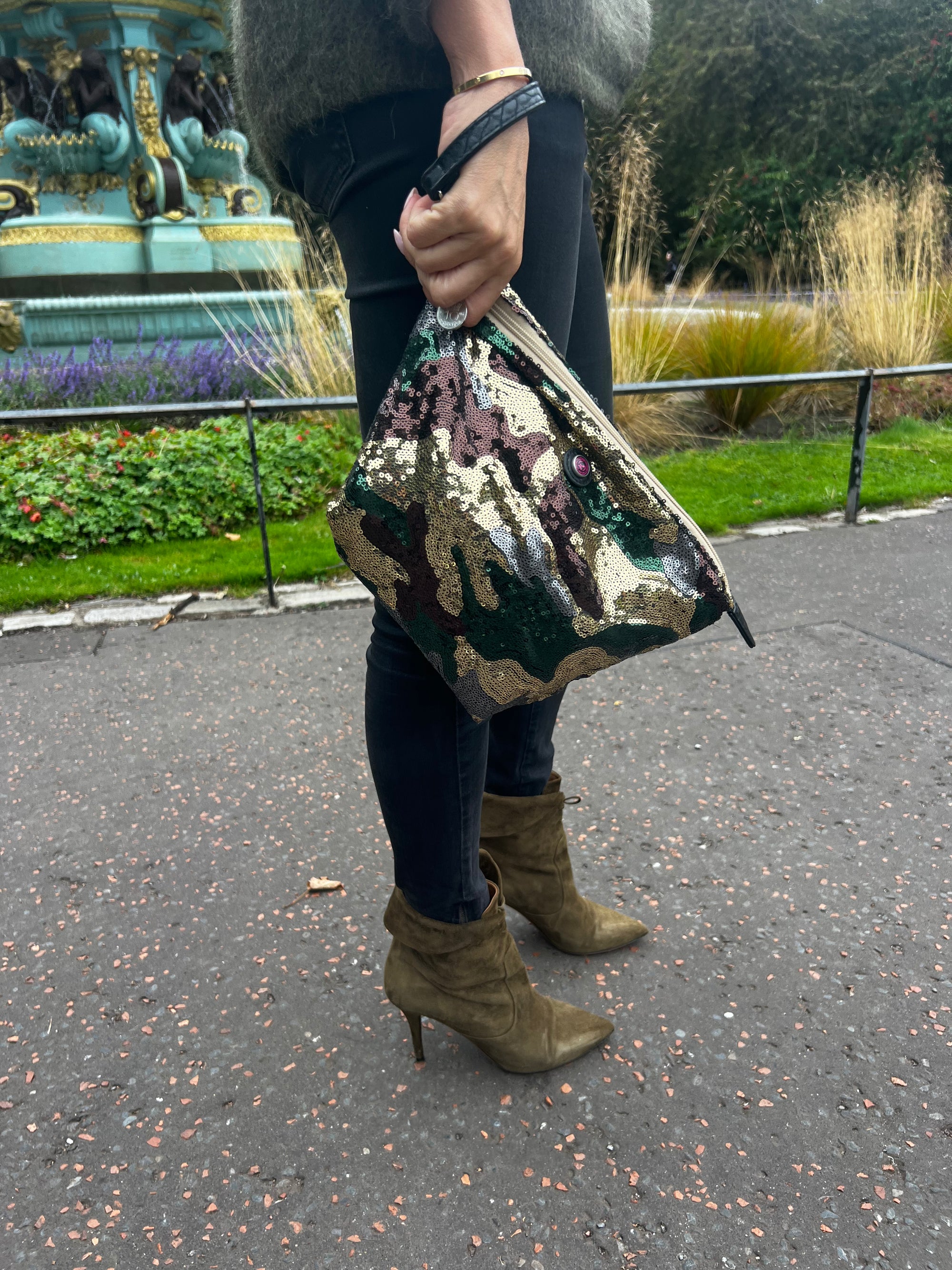 A toiletry bag ion hand with an army print and sequins, predominantly green, brown, and beige.