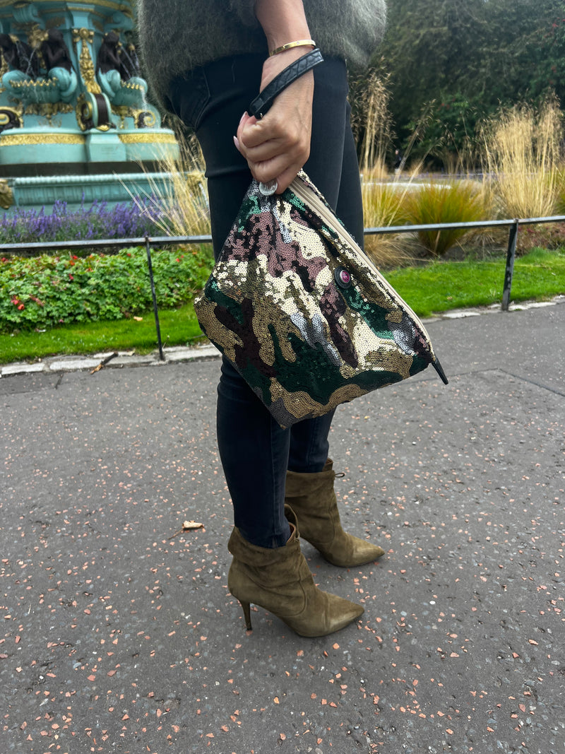 A toiletry bag ion hand with an army print and sequins, predominantly green, brown, and beige.