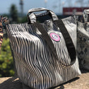 Close-up of a mini zebra shopper with black handles, outdoors on a stone ledge