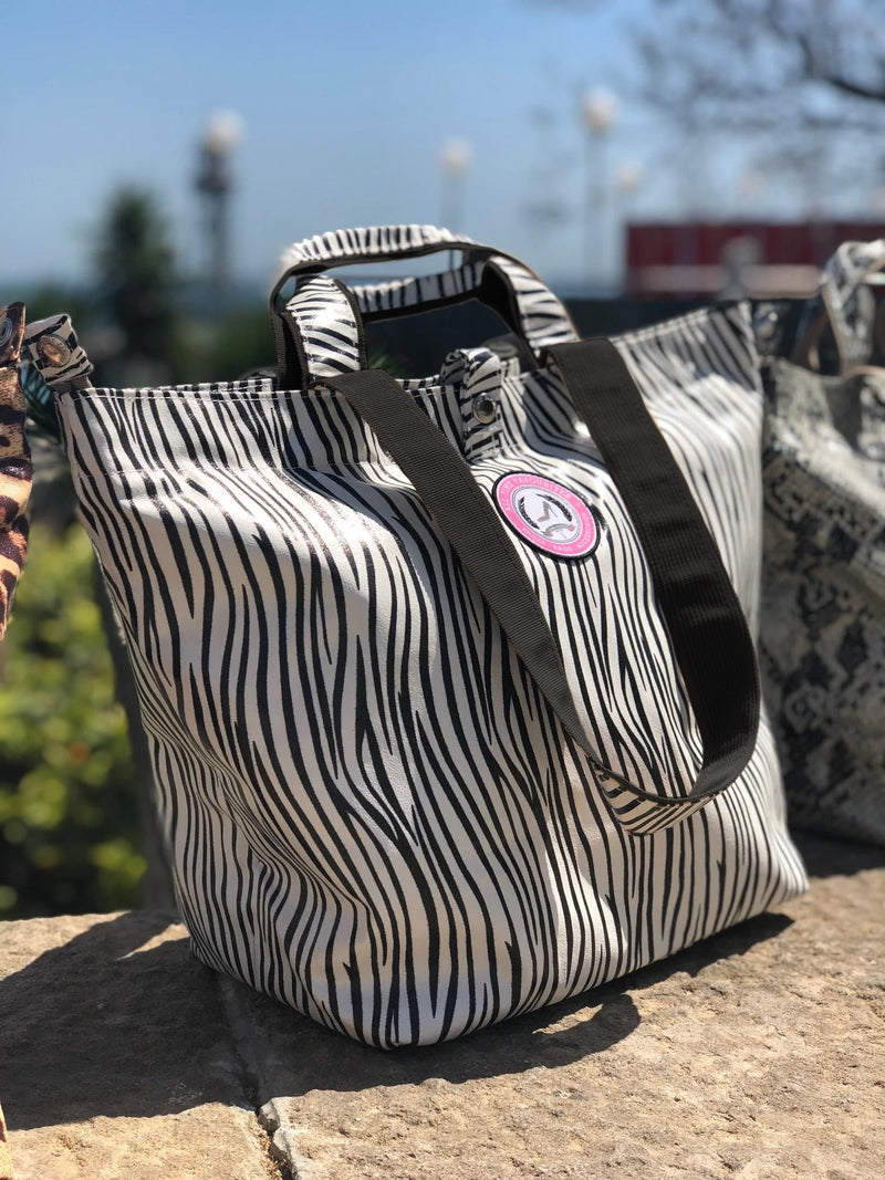 Close-up of a mini zebra shopper with black handles, outdoors on a stone ledge