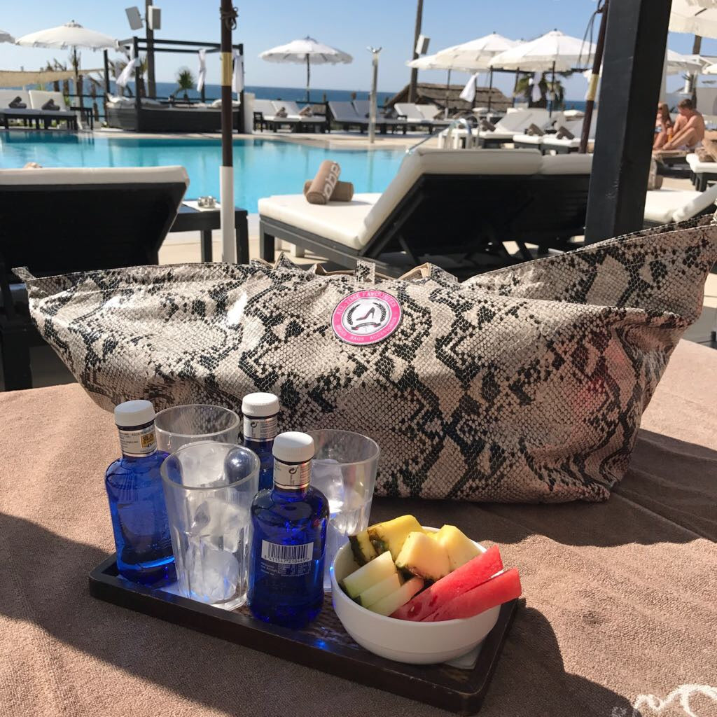 Grote shopper pythonprint op ligbed bij zwembad met fruit en drankjes