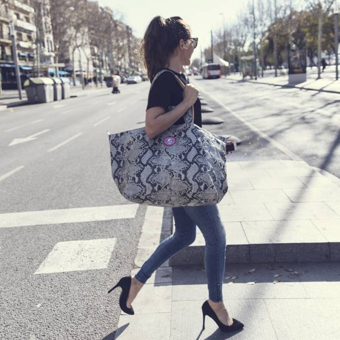 Vrouw loopt over zebrapad met kleine shopper in pythonprint aan haar arm