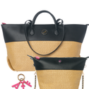 A two-tone tote bag with a black faux-leather top section and a natural beige woven straw bottom, shown alongside a matching zip pouch and a pink keychain on a white background.