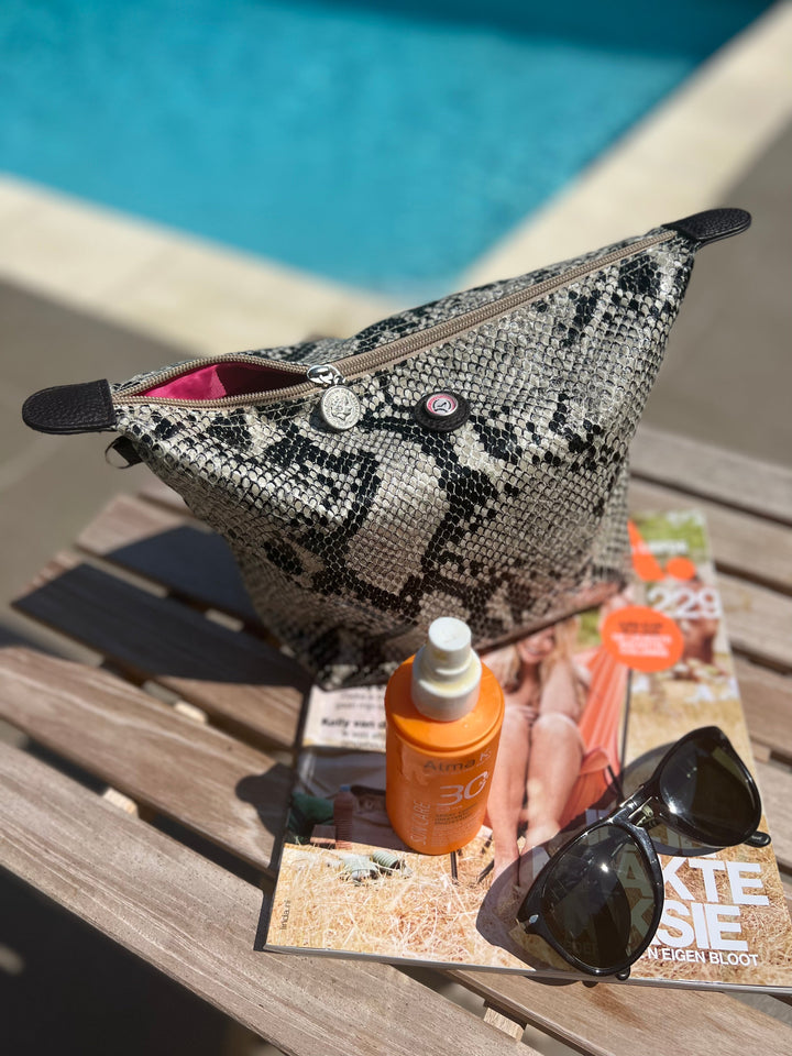 Python-bedruckte Kulturtasche mit Sonnencreme, Sonnenbrille und einer Zeitschrift auf einem Holztisch am Pool.