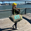 Woman wearing an ATF khaki canvas tote bag on a city boardwalk with river and bridges in the background