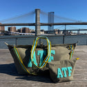 ATF canvas tote bag with matching toiletry bag on a wooden boardwalk, city bridge in the background