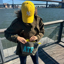 Woman opening an ATF canvas toiletry bag on a city boardwalk with river and bridges in the background