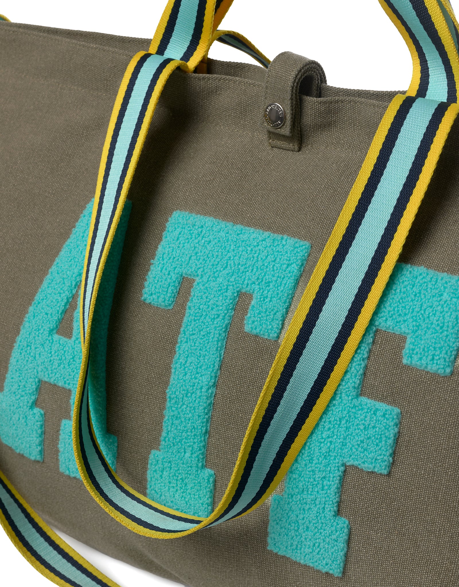 Close-up of ATF logo embroidery on canvas tote bag with striped shoulder straps