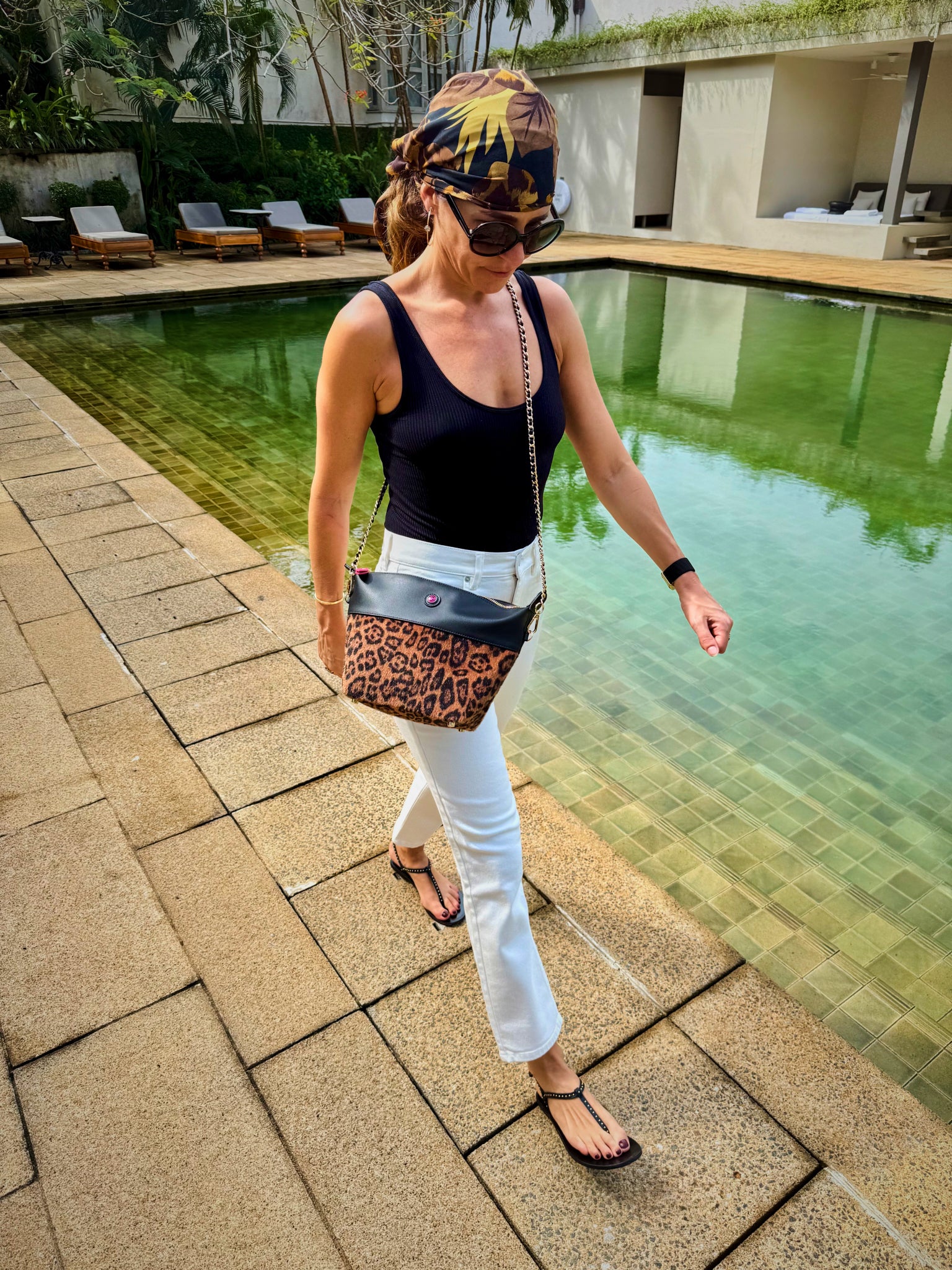 Woman walking by a poolside with a small leopard print crossbody bag