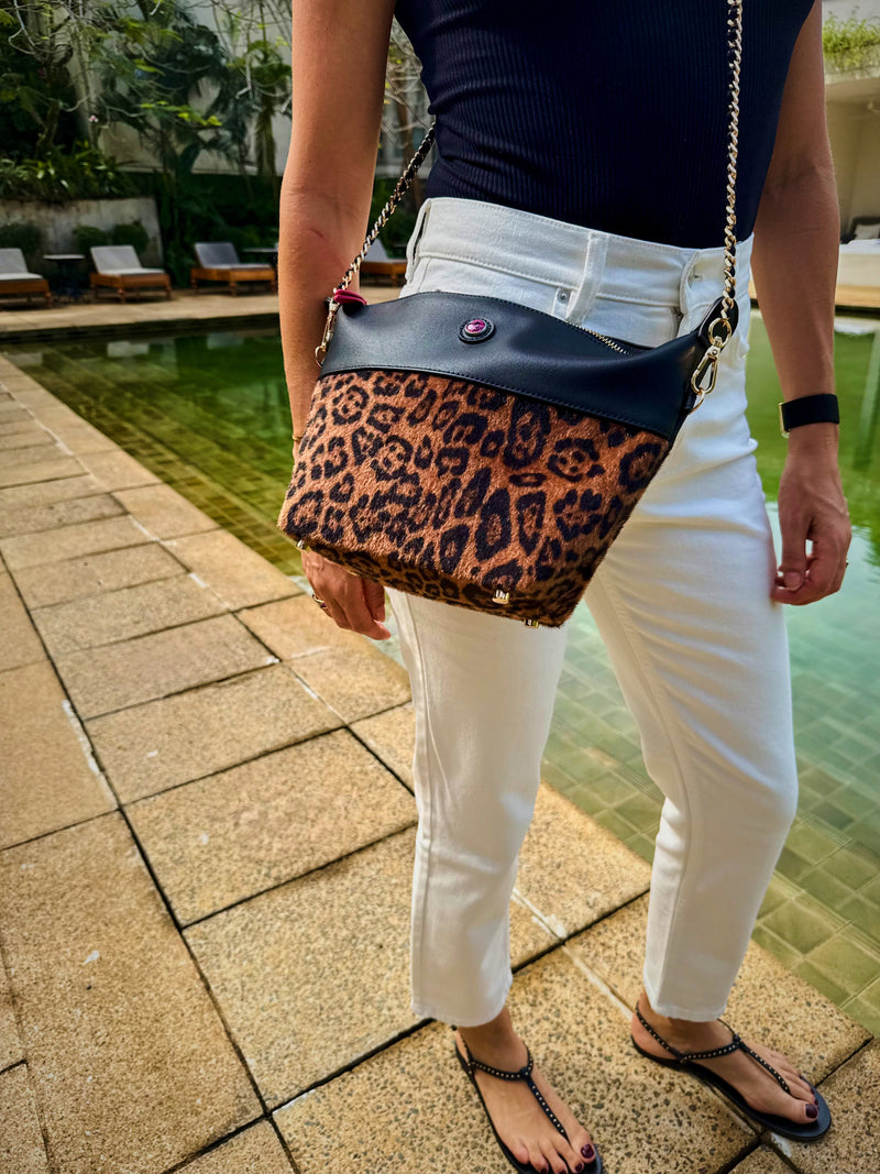 Woman wearing a leopard crossbody bag with gold chain walking by a resort pool