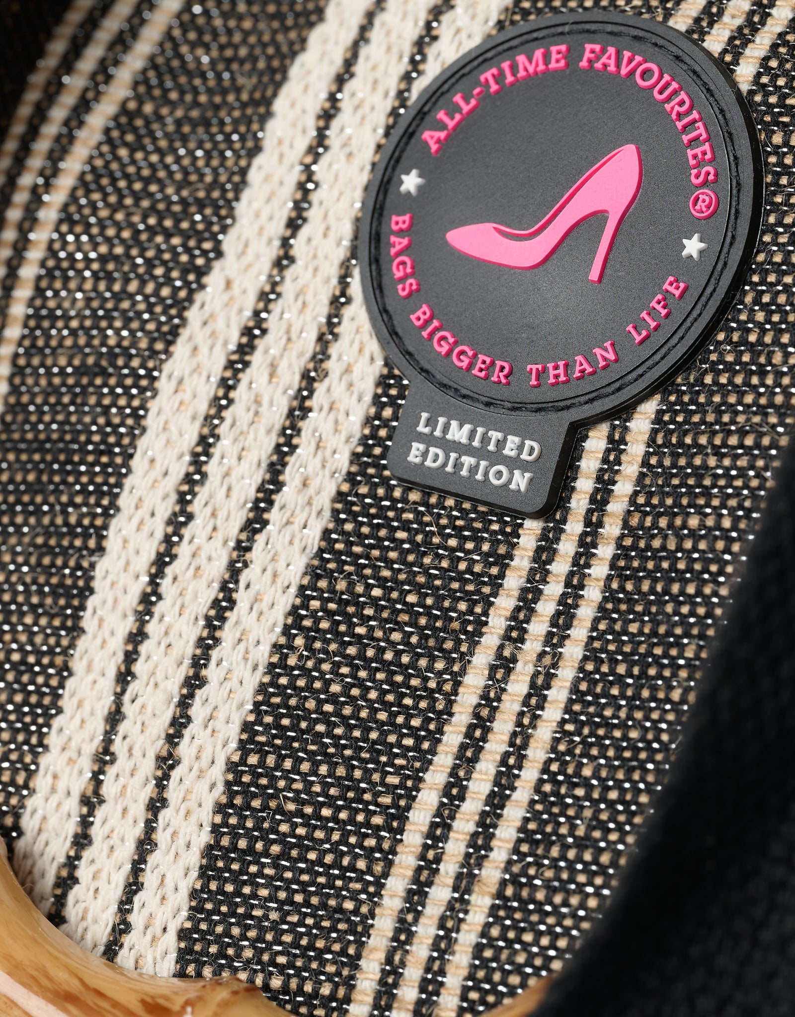 Close-up of a black and white striped tote bag with a 'All-Time Favourites' patch featuring a pink high heel design.