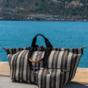 Striped All-time Favourites bag with bamboo handle on a stone surface by a body of water with a mountainous background