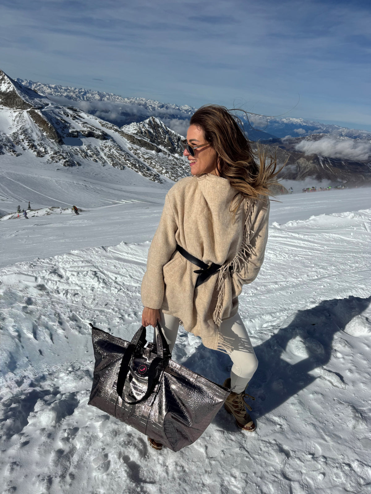 Woman in beige sweater holds bronze metallic BRIGITTE large tote bag on snowy mountain backdrop.