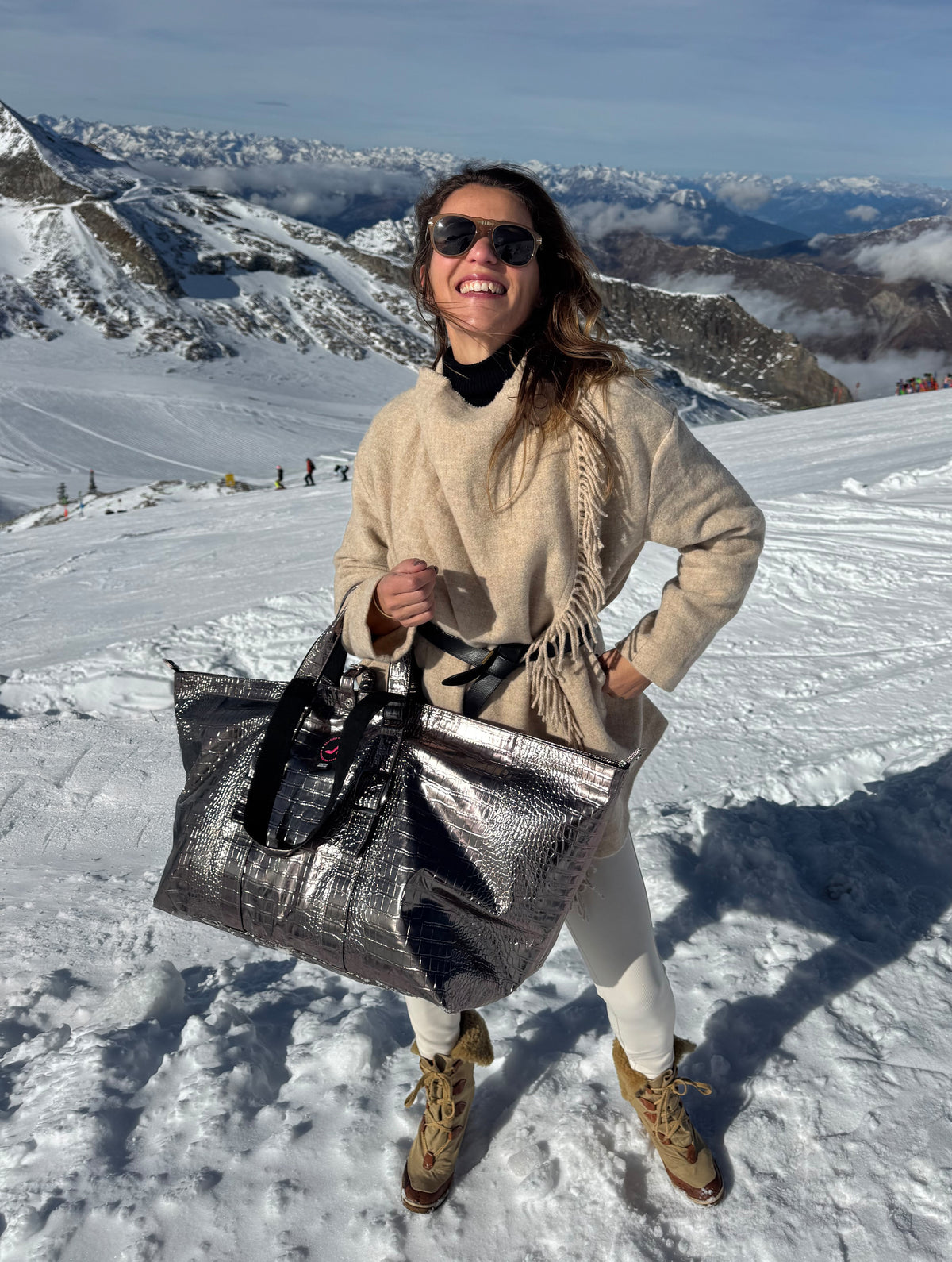 Woman in beige sweater holds taupe leather BRIGITTE Large Tote Bag on snowy mountain.