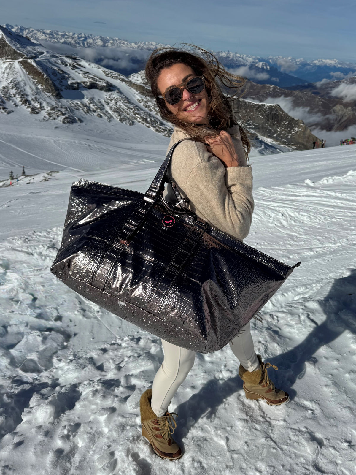Woman in sunglasses on snowy mountain carries bronze metallic BRIGITTE Large Tote Bag by All-time Favourites.