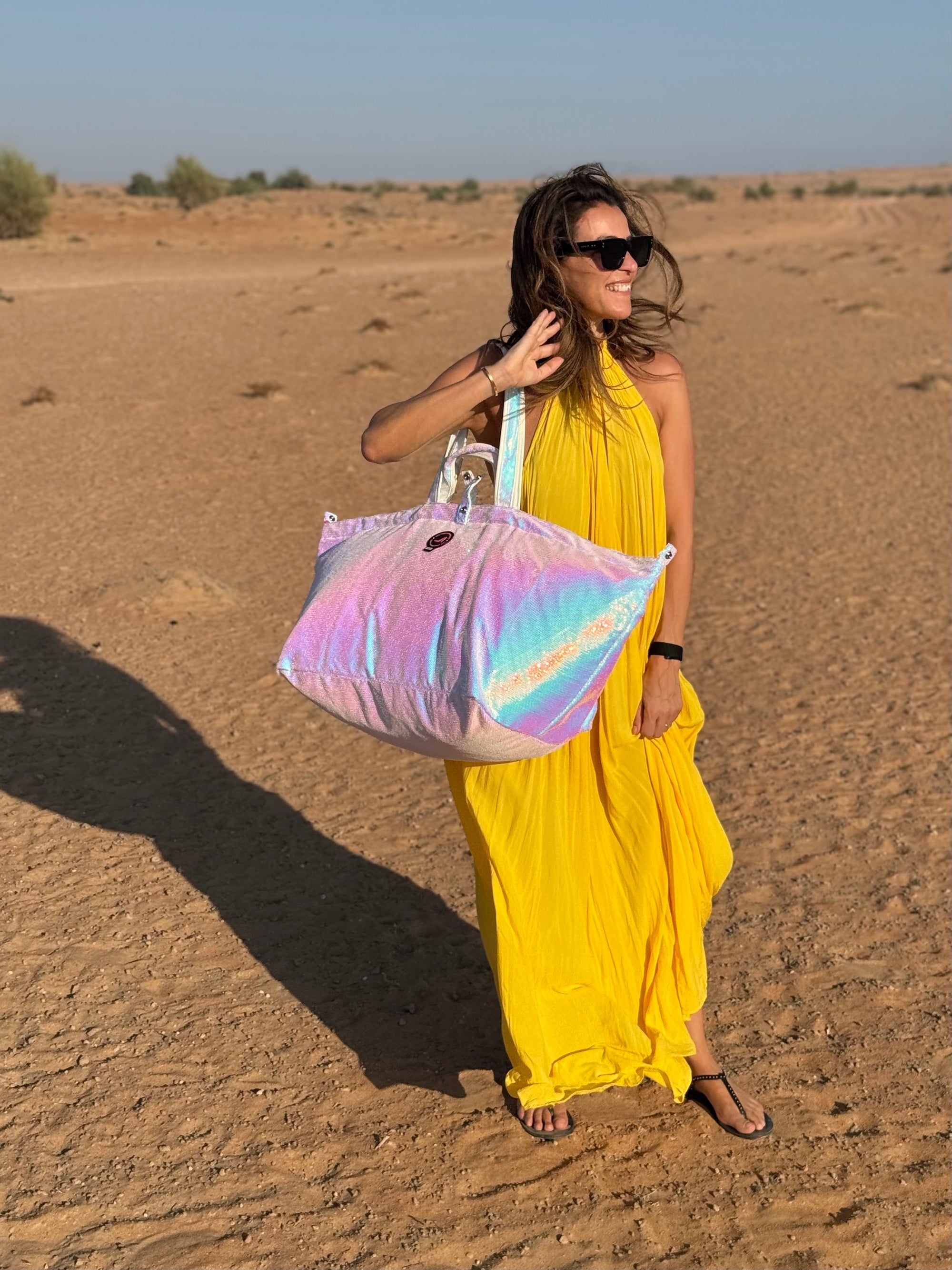 Woman in a yellow dress holding a colorful sequin large tote bag in a desert setting