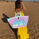 Person in a yellow dress holding a colorful iridescent large tote bag in a desert setting