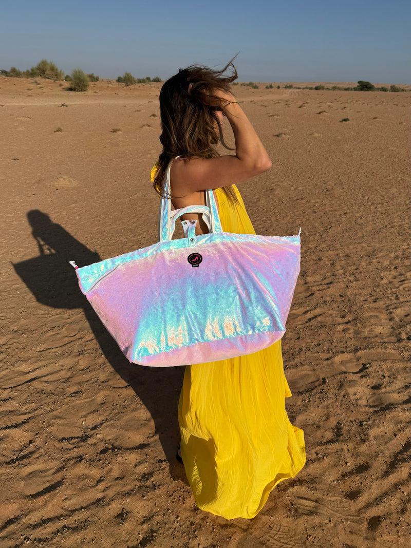 Person in a yellow dress holding a colorful iridescent large tote bag in a desert setting