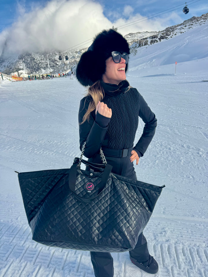 Woman in black winterwear on snowy slope carrying KATE All-time Favourites Large Tote Bag in Black Caviar leather.