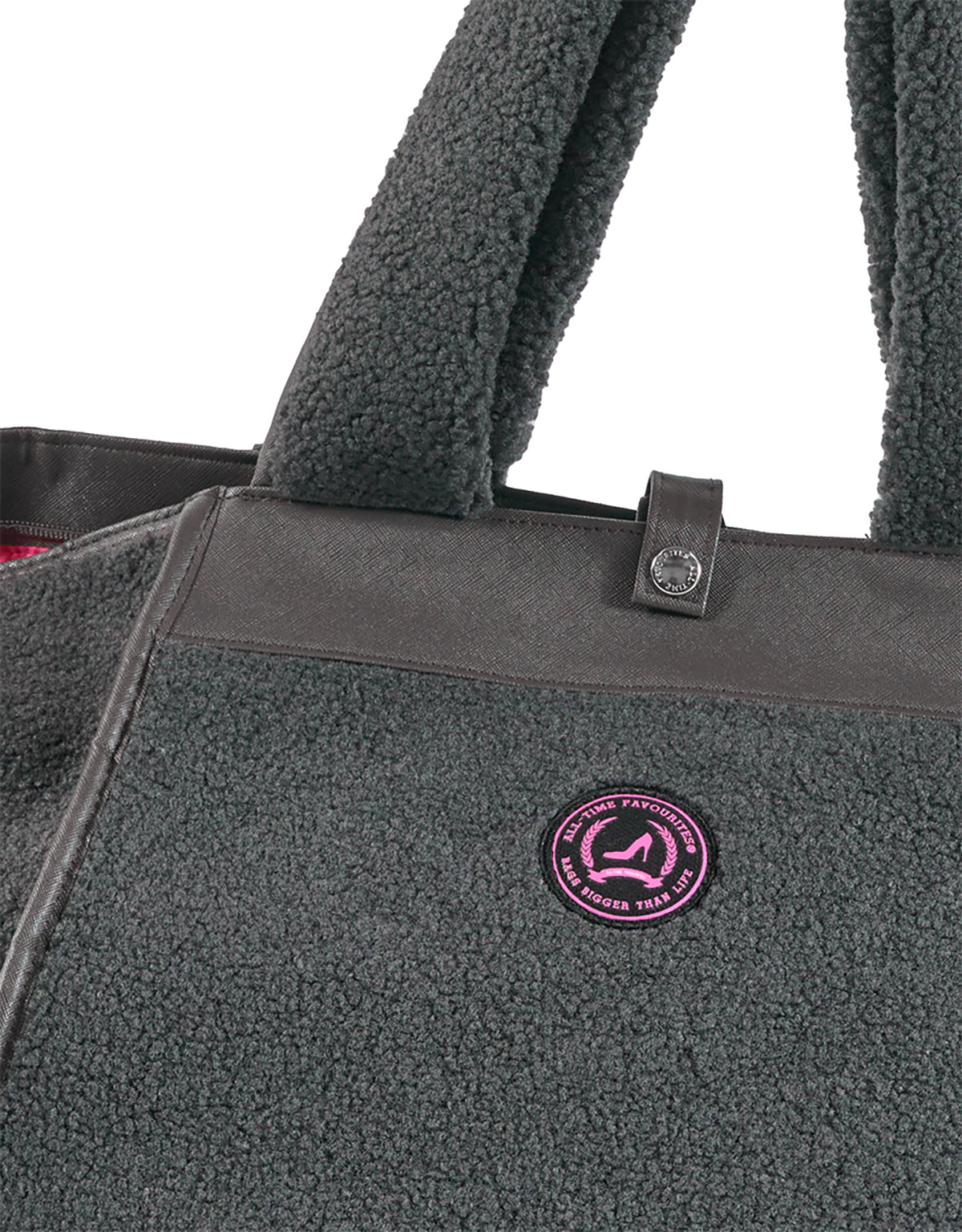 Mittelgraue Teddy-Tragetasche mit breiten Henkeln und einem runden, rosa Logo-Aufnäher auf der Vorderseite.