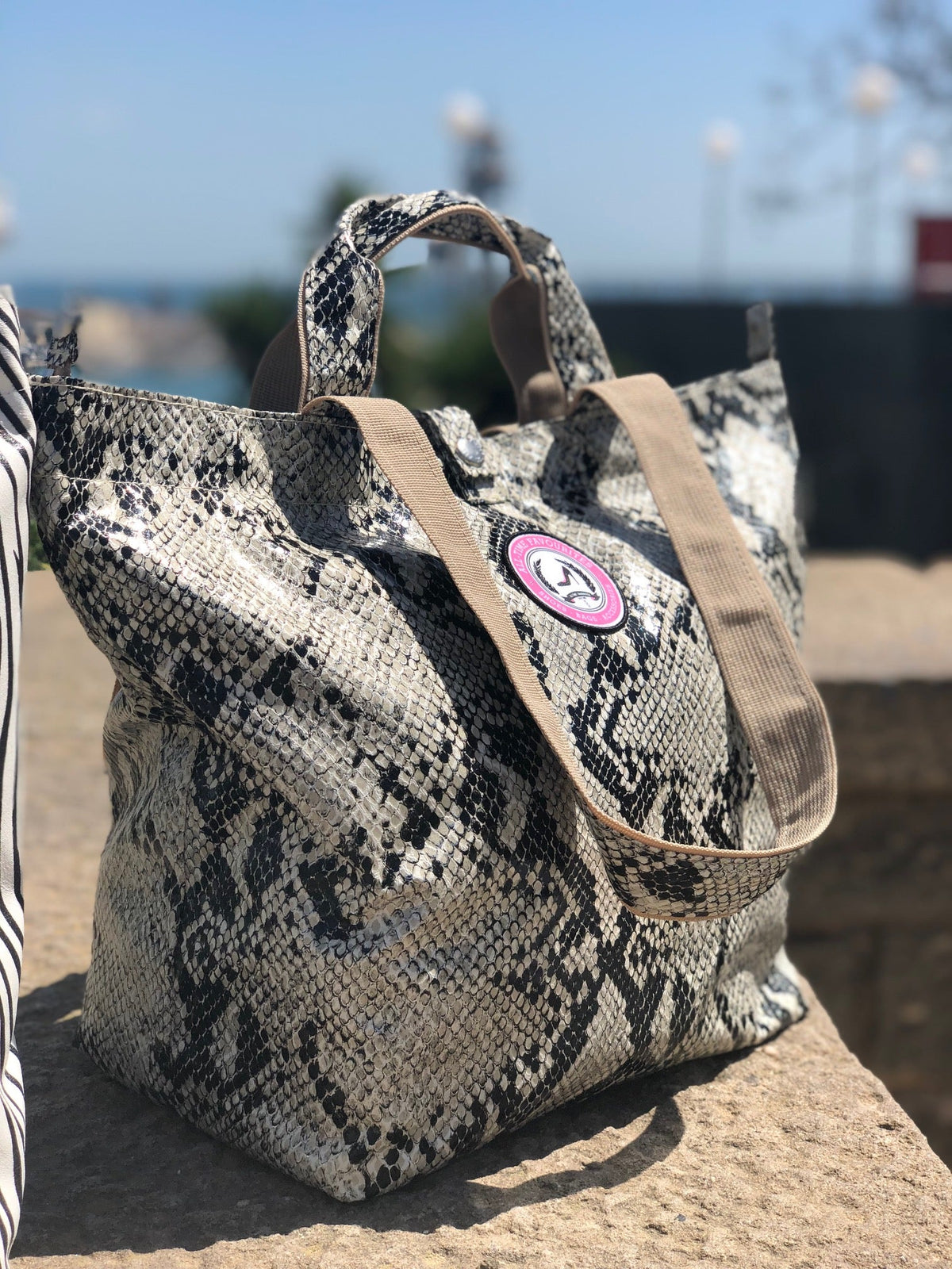 Kleine draagtas met pythonprint en bruinbeige hengsels van All-time Favourites op een zonovergoten stenen ondergrond.
