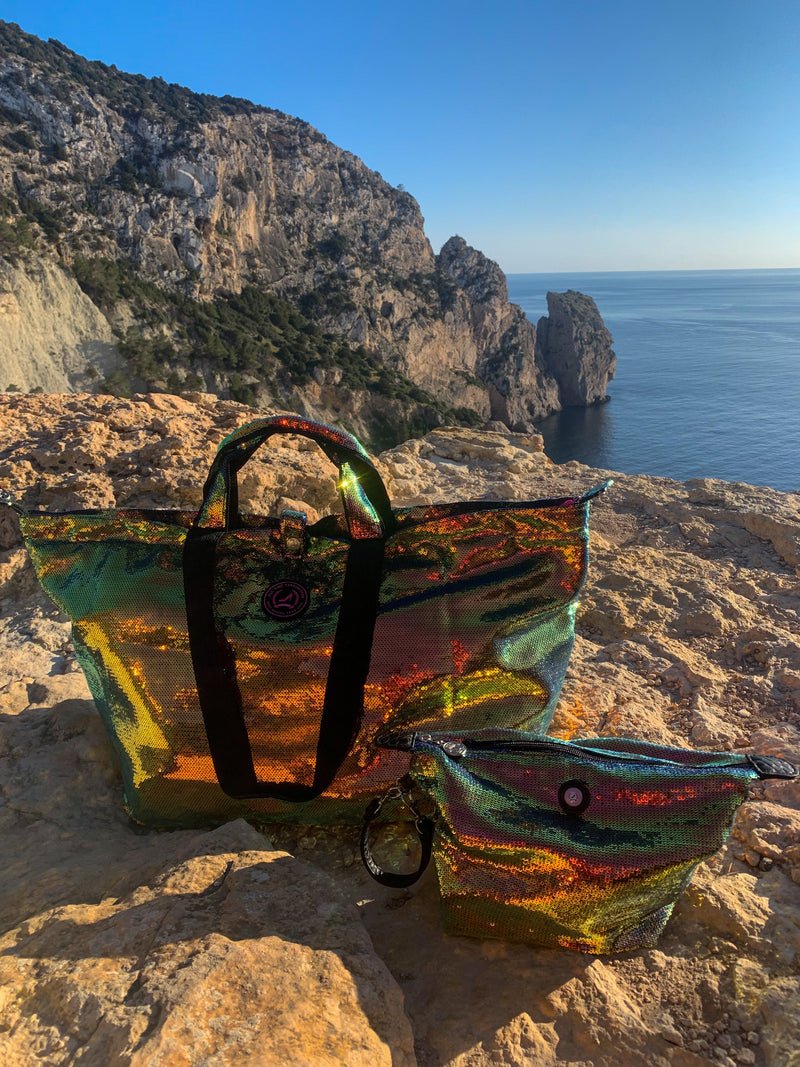 Multicolored sequin tote bag and matching toiletry bag placed on rocky cliffs overlooking the sea