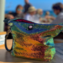 Multicolored sequin toiletry bag with zipper on a wooden table, beach setting in the background