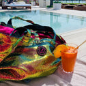 Large multi coloured sequin tote bag on a lounge bed with a pool in the background