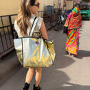 Woman with a reflective gold tote bag walking on a street in India with a colorful saree-wearing woman in the background.
