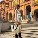 Woman holding a golden tote bag, standing in front of a colorful building in India with intricate architecture