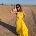 Woman in a yellow dress standing on a sandy surface with a clear blue sky showing a small white key pouch