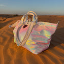 Iridescent large tote bag on a sand dune in the desert with a blurred background.”