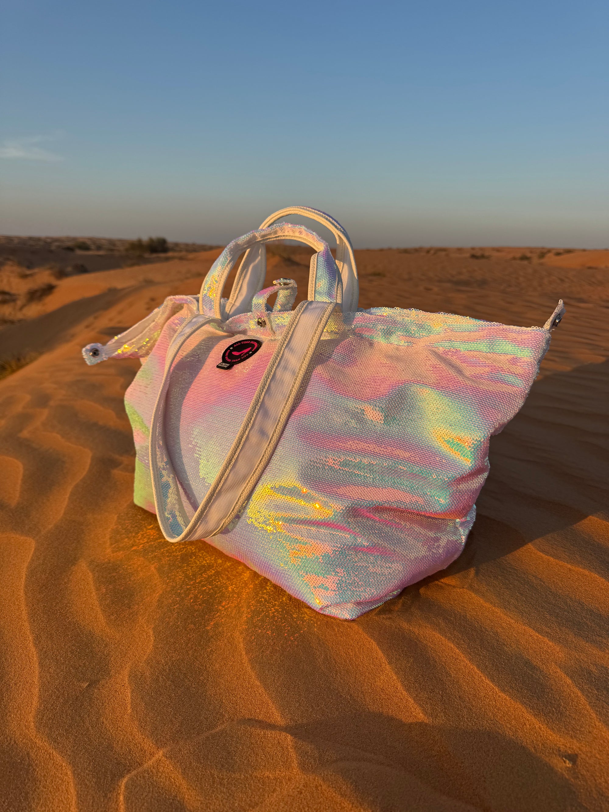 Iridescent large tote bag on a sand dune in the desert with a blurred background.”