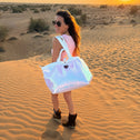 Woman holding a medium sized white sequin tote bag in a desert landscape at sunset