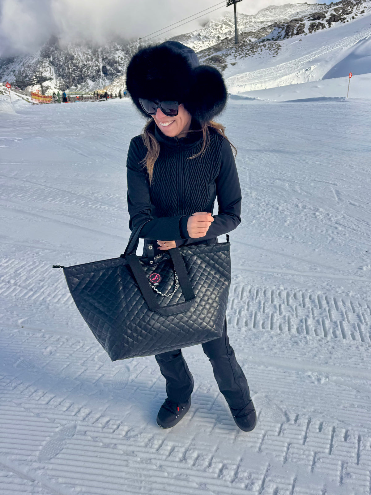 Woman in black winter clothes holding black caviar leather medium tote bag on snowy slopes.