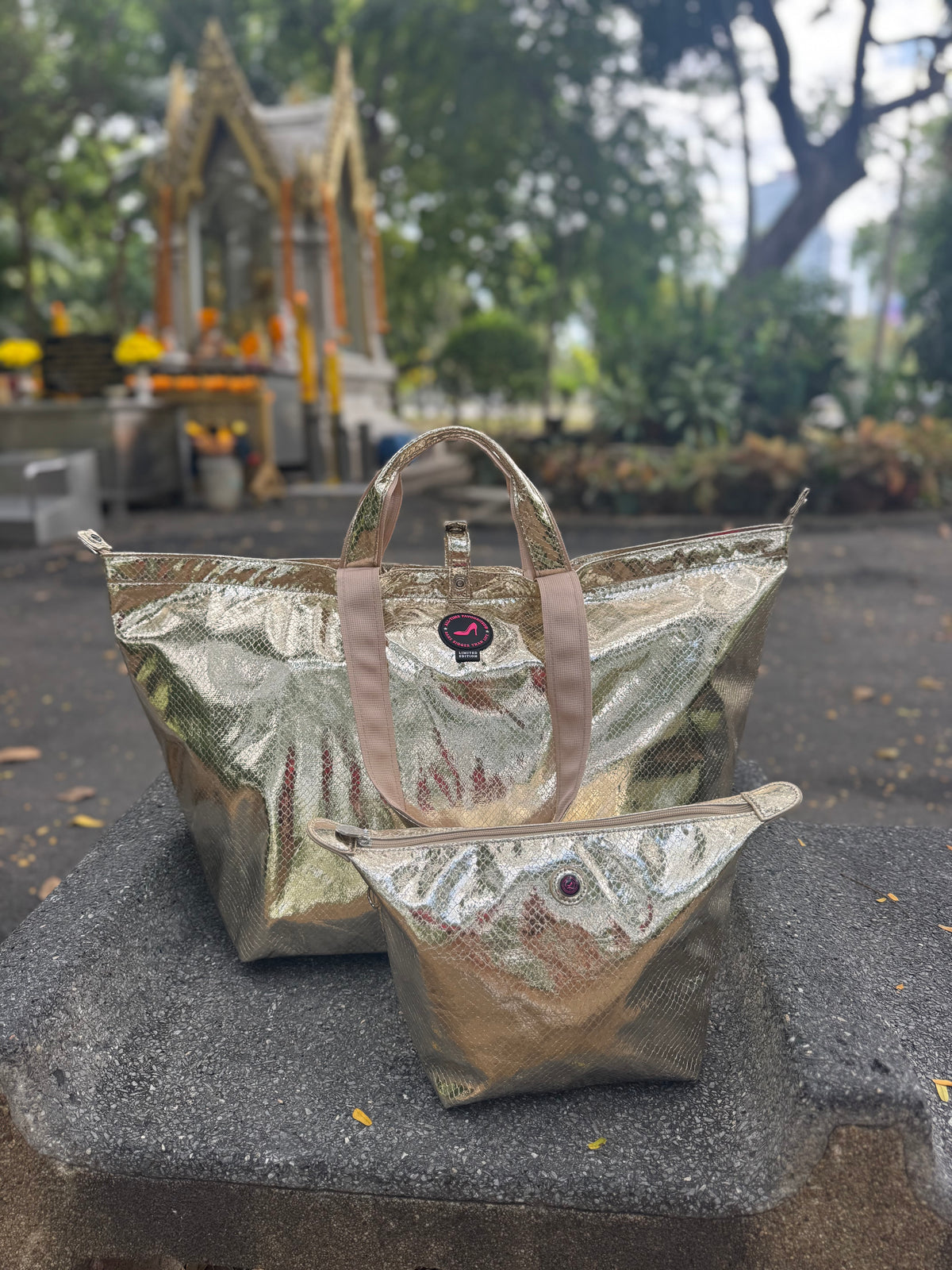 Champagnekleurige, gouden CHIANG MAI-toilettassen van leer op een richel, met op de achtergrond een heiligdom en bomen.