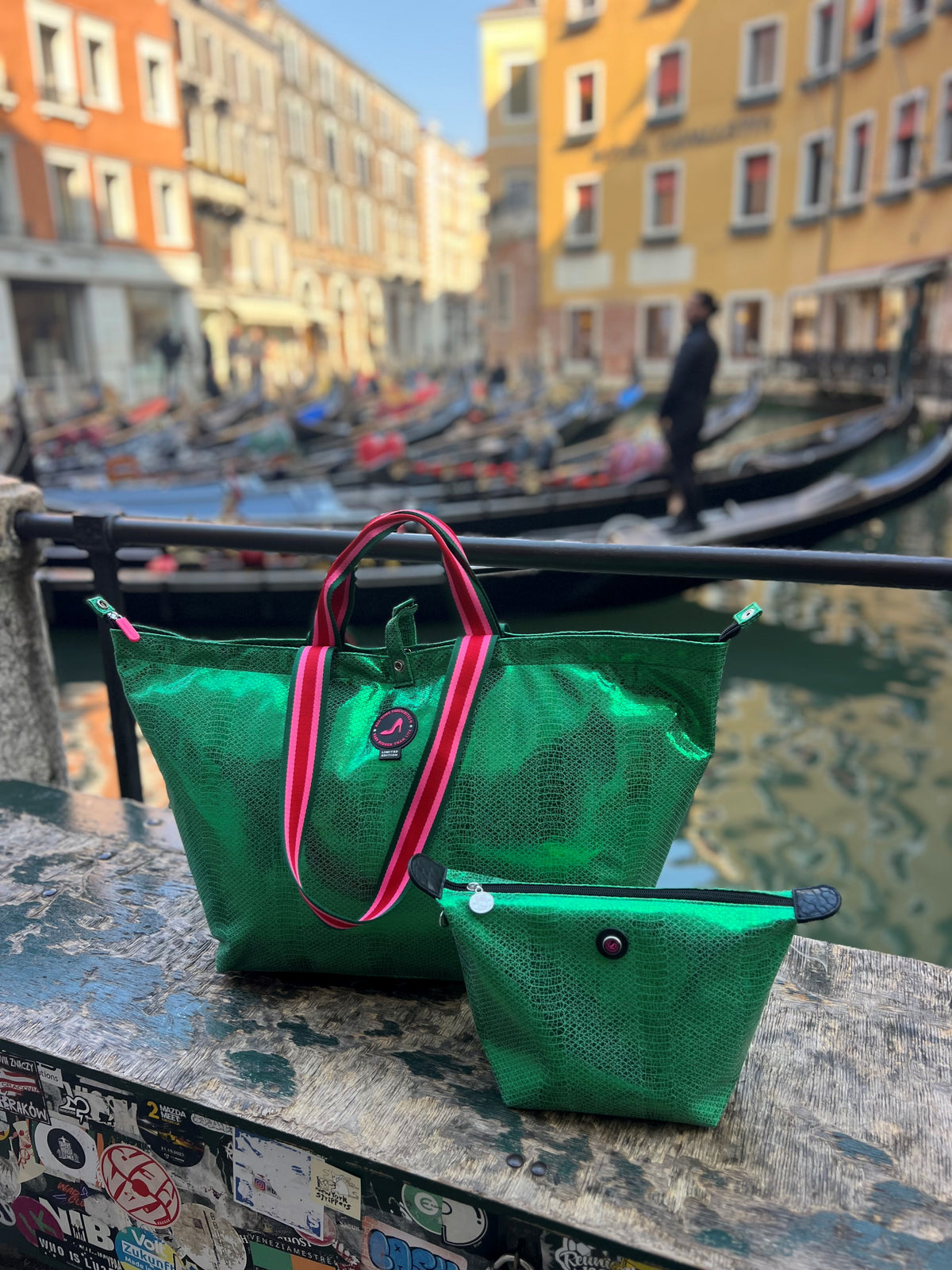 Metallic green Venezia medium tote bag by All-time Favourites on graffiti-covered ledge beside canal.
