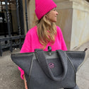 Woman with large grey teddy shopper bag with two handles, zipper closure and round pink logo on the front