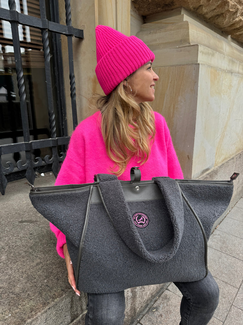 Woman with large grey teddy shopper bag with two handles, zipper closure and round pink logo on the front