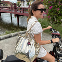 Woman riding a scooter carrying a small  champagne gold metallic tote bag with python texture
