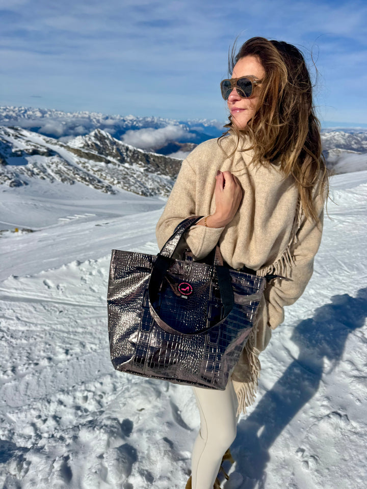Woman in sunglasses and beige outfit on snowy mountain holding bronze metallic small tote bag BRIGITTE.