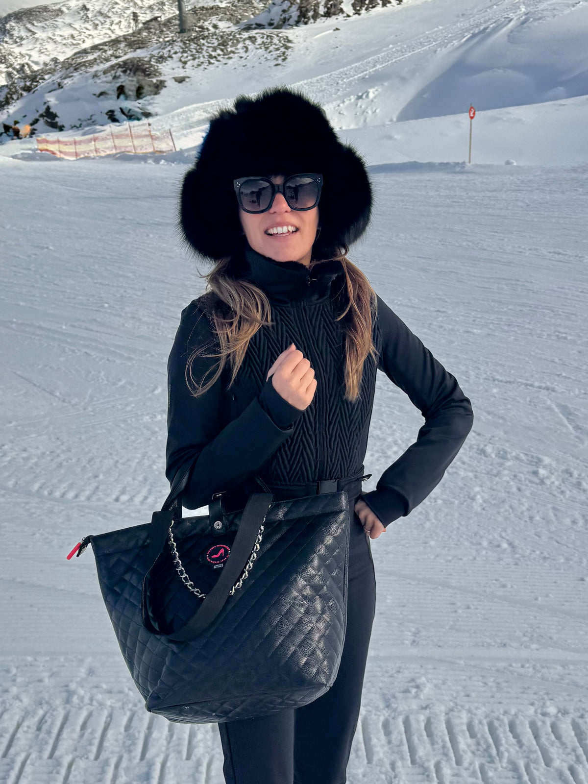 Woman in black and fur hat holding black caviar leather KATE All-time Favourites Small Tote Bag on snowy slope.