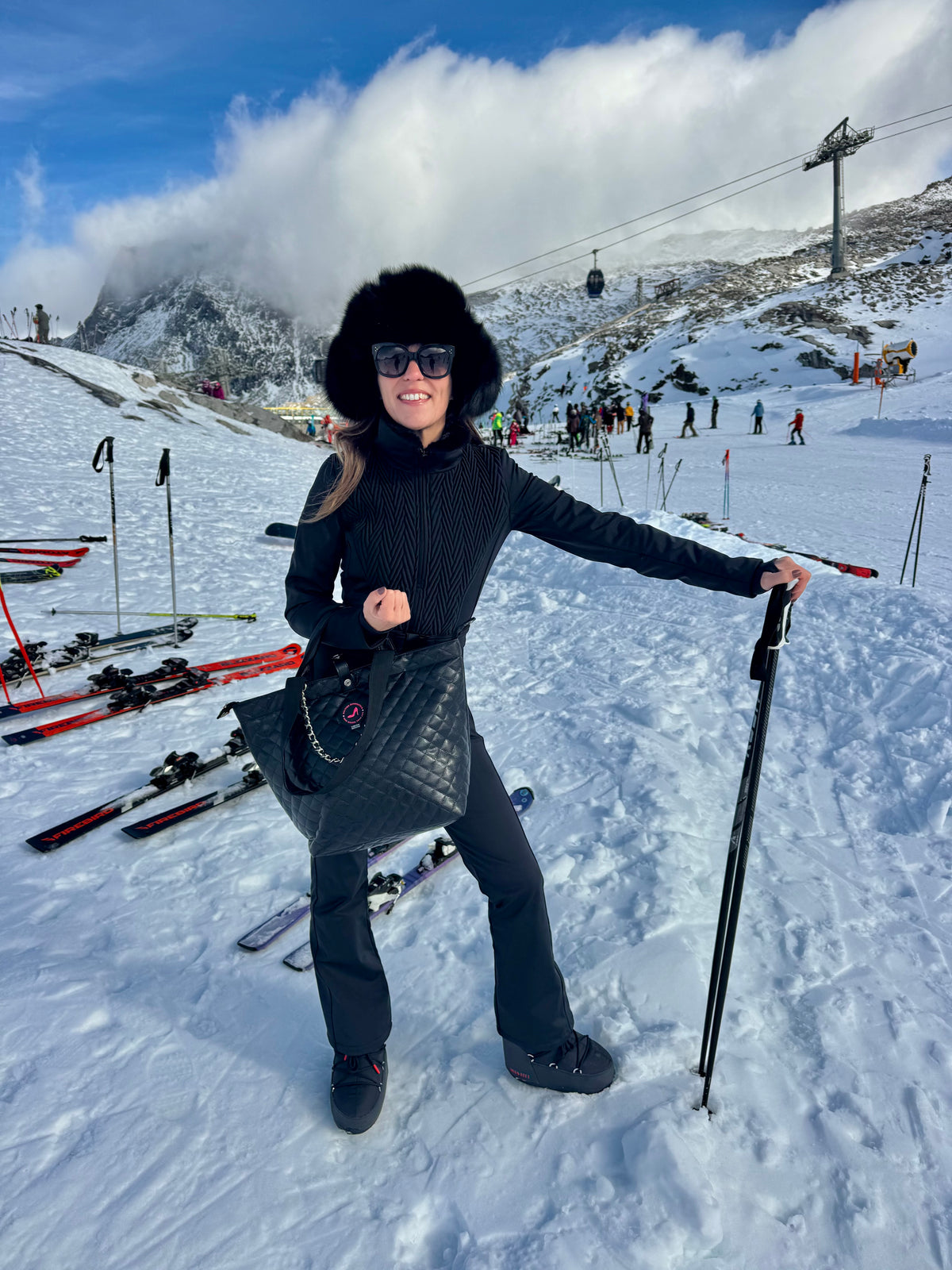 Woman in black winter outfit and fur hat on snowy slope holding black caviar small tote bag by KATE.