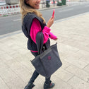 Happy woman walking in the street wearing a small grey teddy tote bag with zipper and pink logo