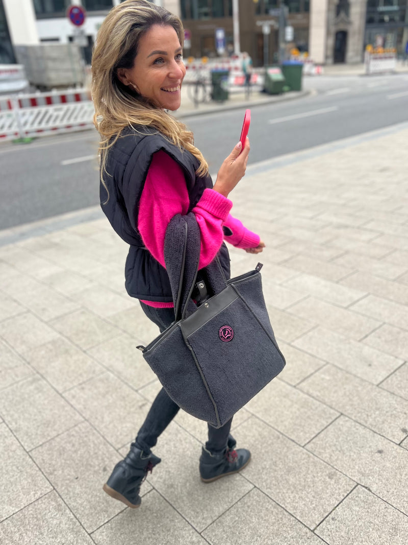 Happy woman walking in the street wearing a small grey teddy tote bag with zipper and pink logo