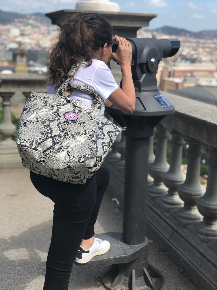 Eine Frau mit einer kleinen Tragetasche mit Python-Muster steht vor einem Stadtpanorama, aus der Vogelperspektive gesehen.